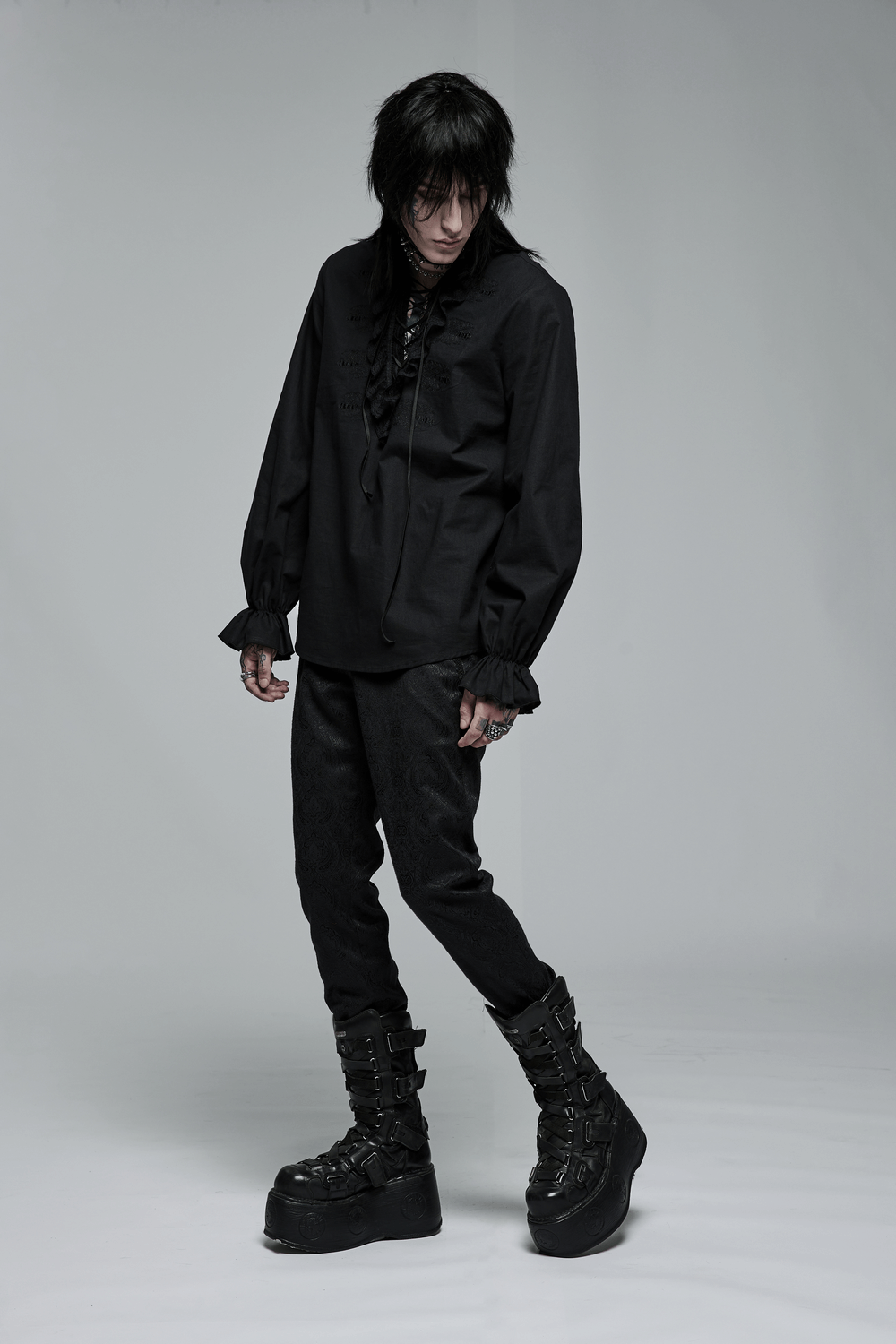 Model wearing a gothic-inspired black shirt with lace details and black platform boots, embodying dark elegance.