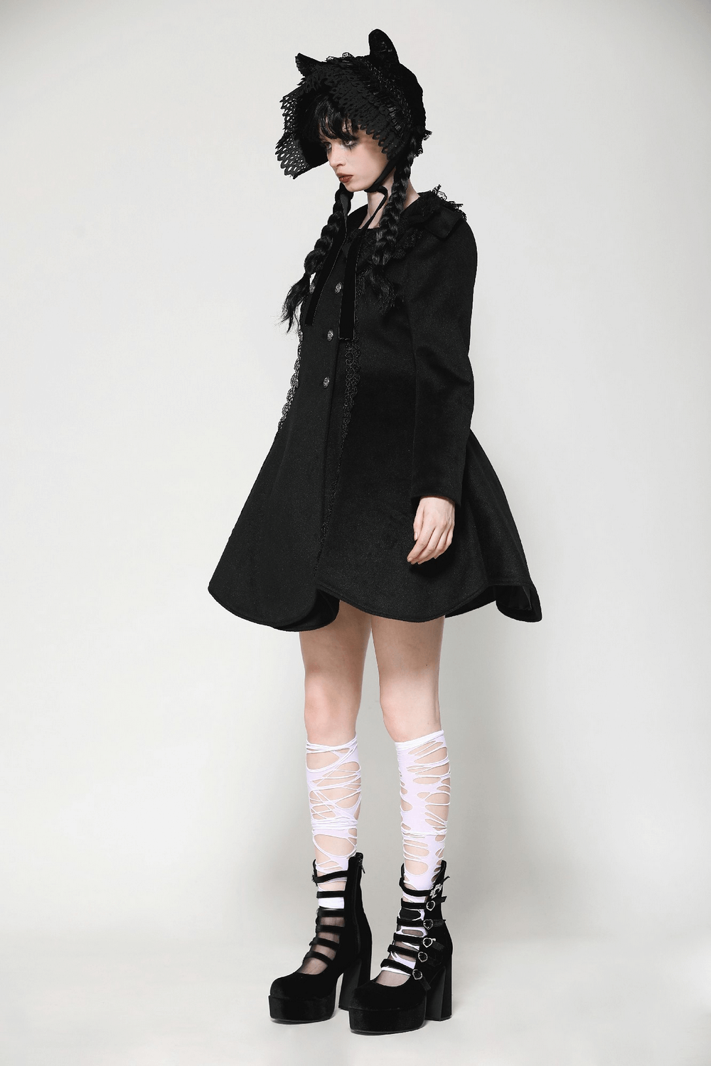 Stylish model in black Victorian-style coat with lace, knee-high socks, and striking platform shoes, embodying elegance.