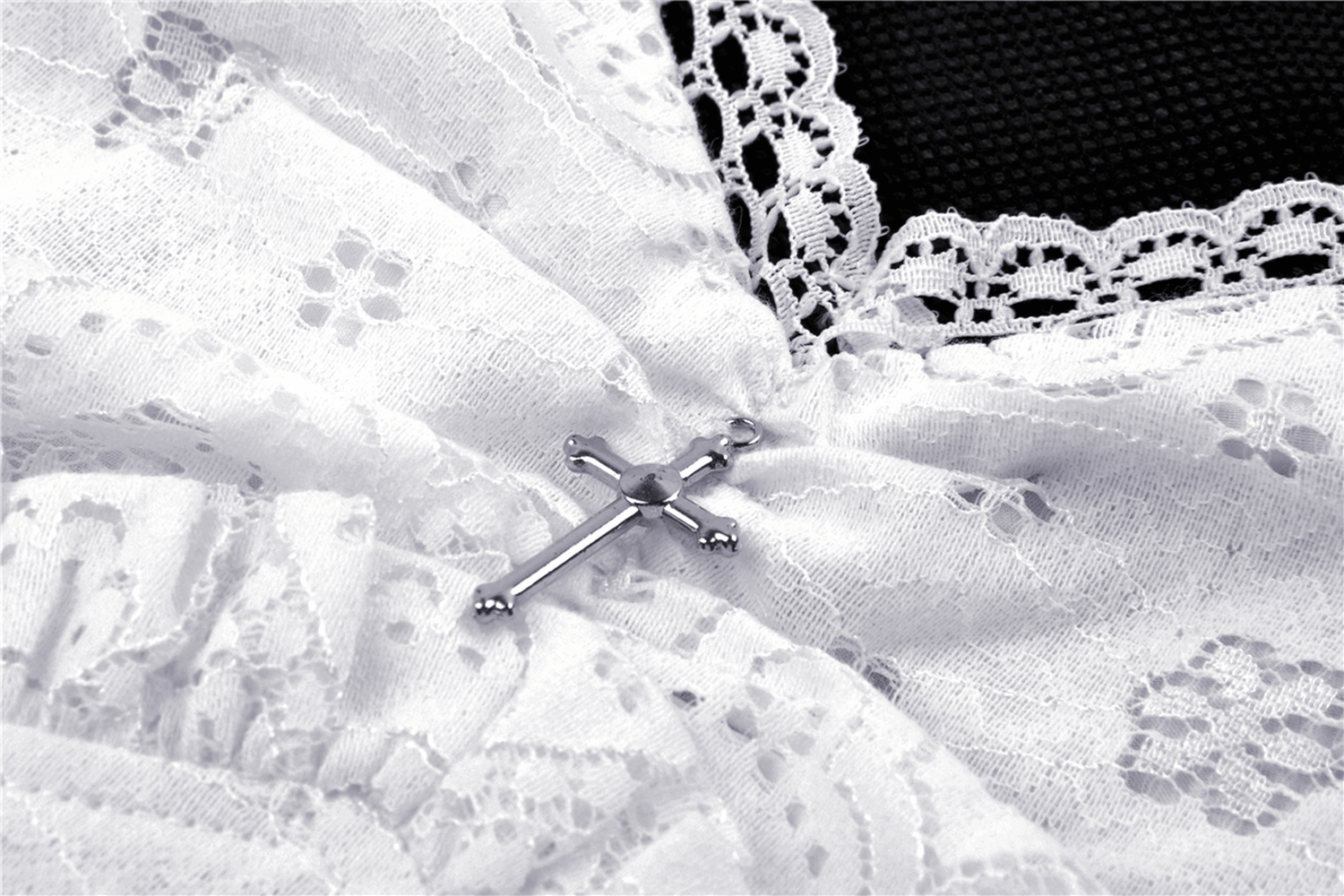 Close-up of white lace fabric with an intricate design and a silver cross accent, perfect for a gothic look.