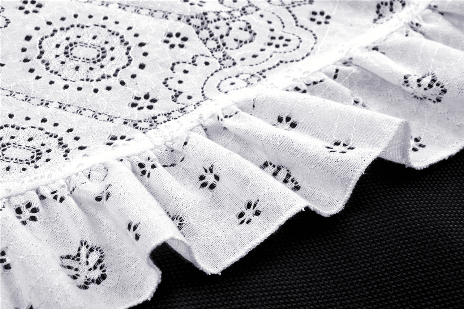 Close-up of intricate white lace with black detailing, showcasing ruffled edges for a gothic dress design.