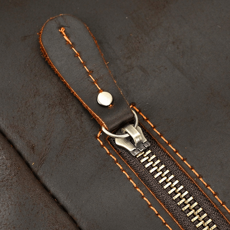 Close-up of a zipper on a large genuine leather backpack with orange stitching accent.