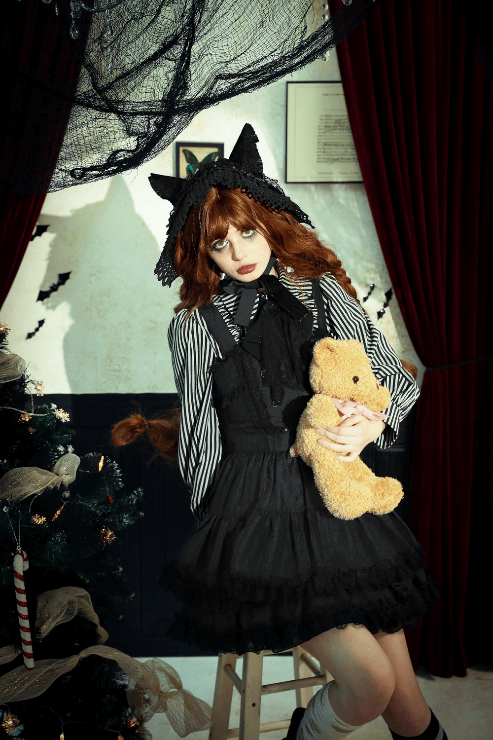 Gothic Lolita dress with lace ruffles, black suspender design, and cute cat ear headband, holding teddy bear in spooky decor.