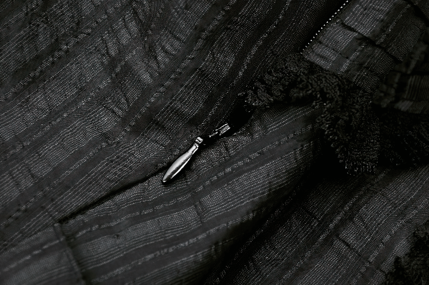 Detailed close-up of the black fabric and zipper featuring lace trim from a gothic Lolita dress.