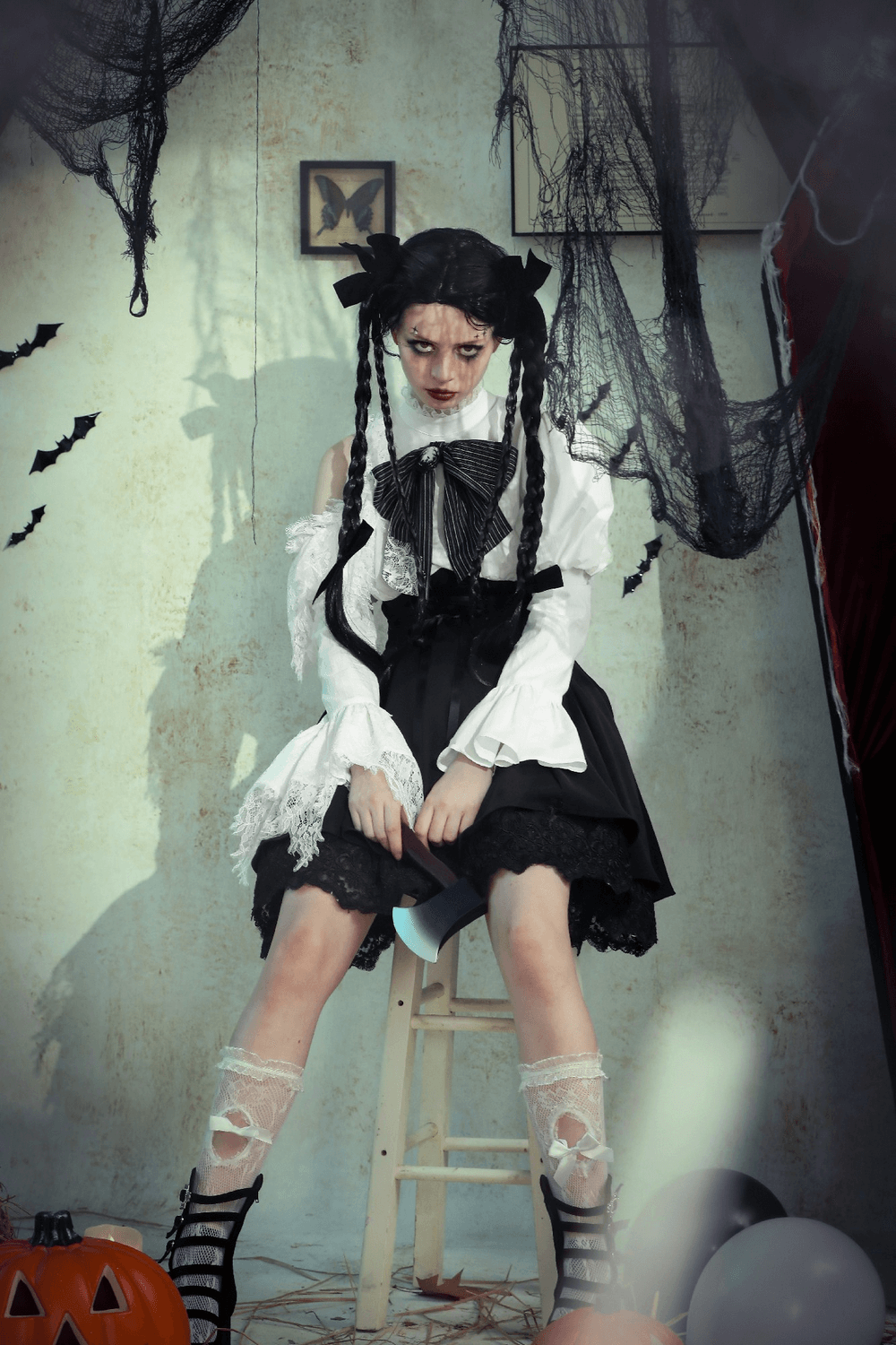 Gothic Lolita girl in black and white dress with lace accents, posing in a spooky setting with Halloween decor.