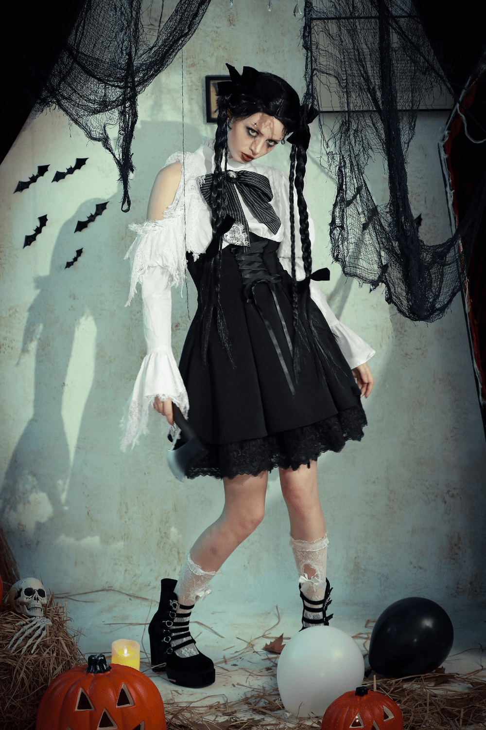 Model in elegant black and white Lolita dress with lace sleeves posing in a gothic Halloween setting.