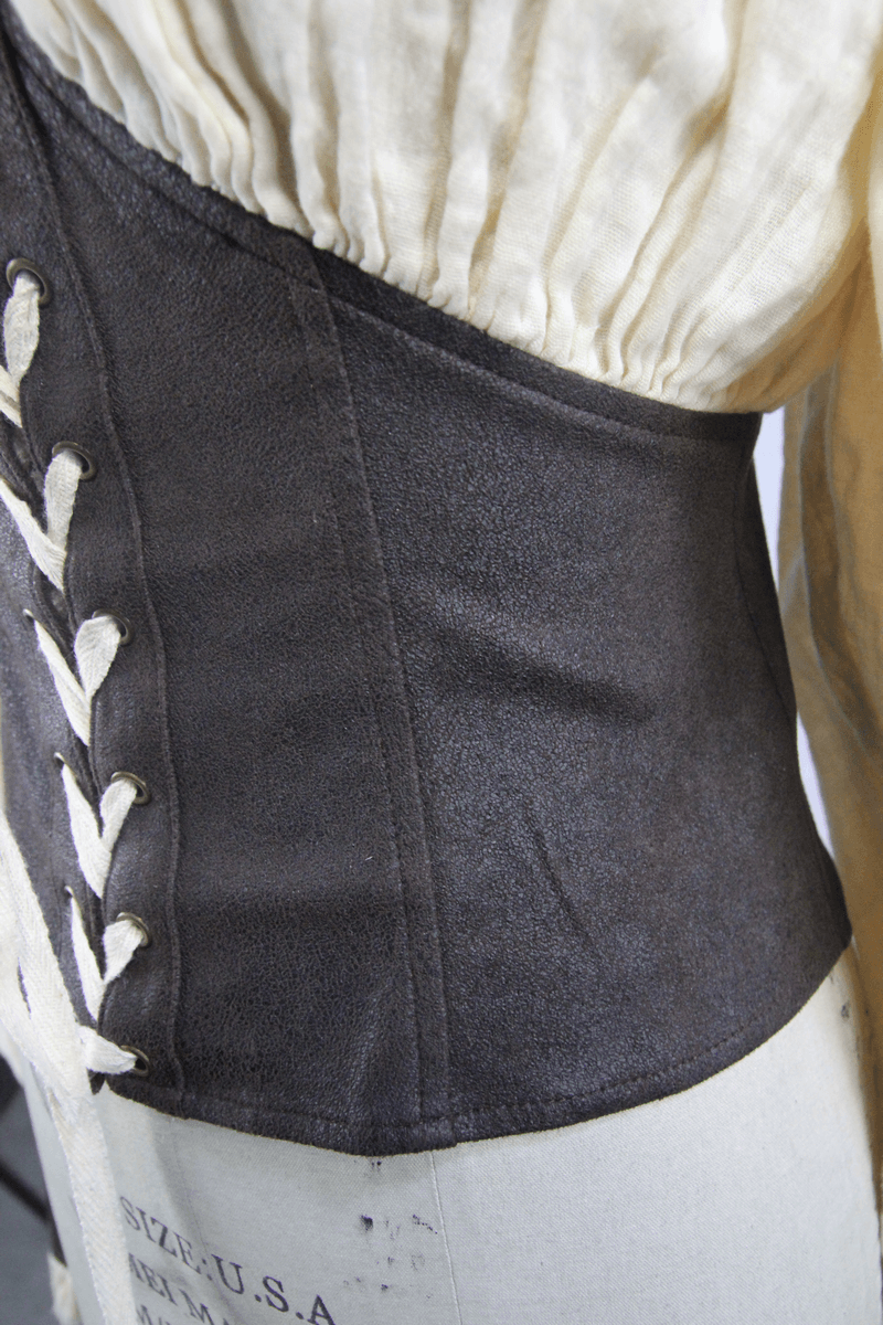 Close-up of vintage beige blouse with decorative brown lacing and structured waist detail, showcasing alternative style fashion.