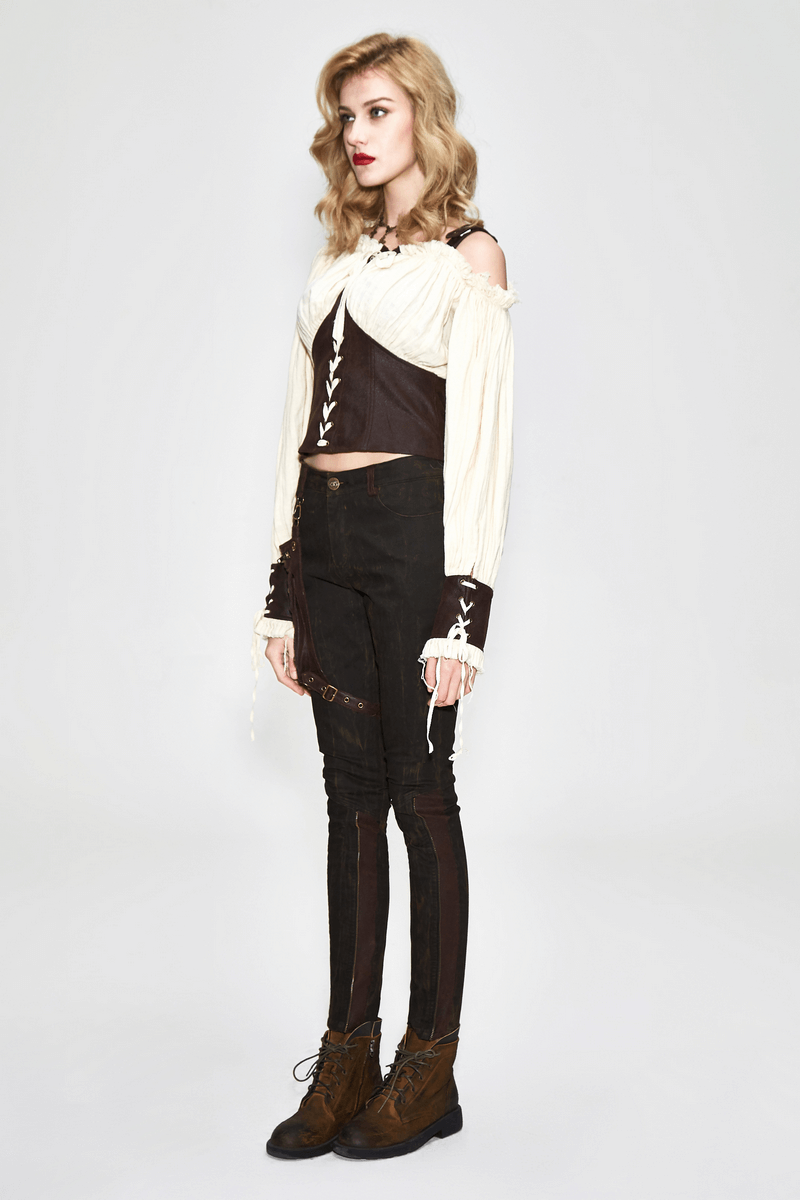 Woman in a beige vintage blouse with lacing, off-one-shoulder style, paired with black pants and brown boots.