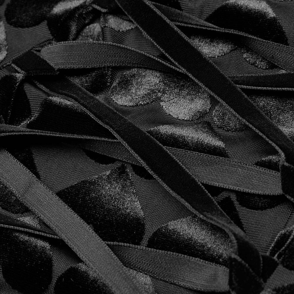 Close-up of black velvet fabric with intricate heart patterns and ribbon details for gothic dress design.