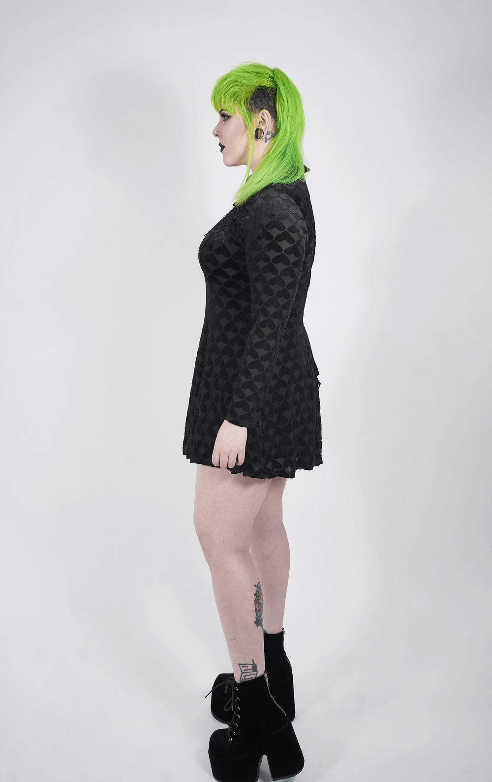 Side view of a model in a black gothic dress with unique textures and vibrant green hair.