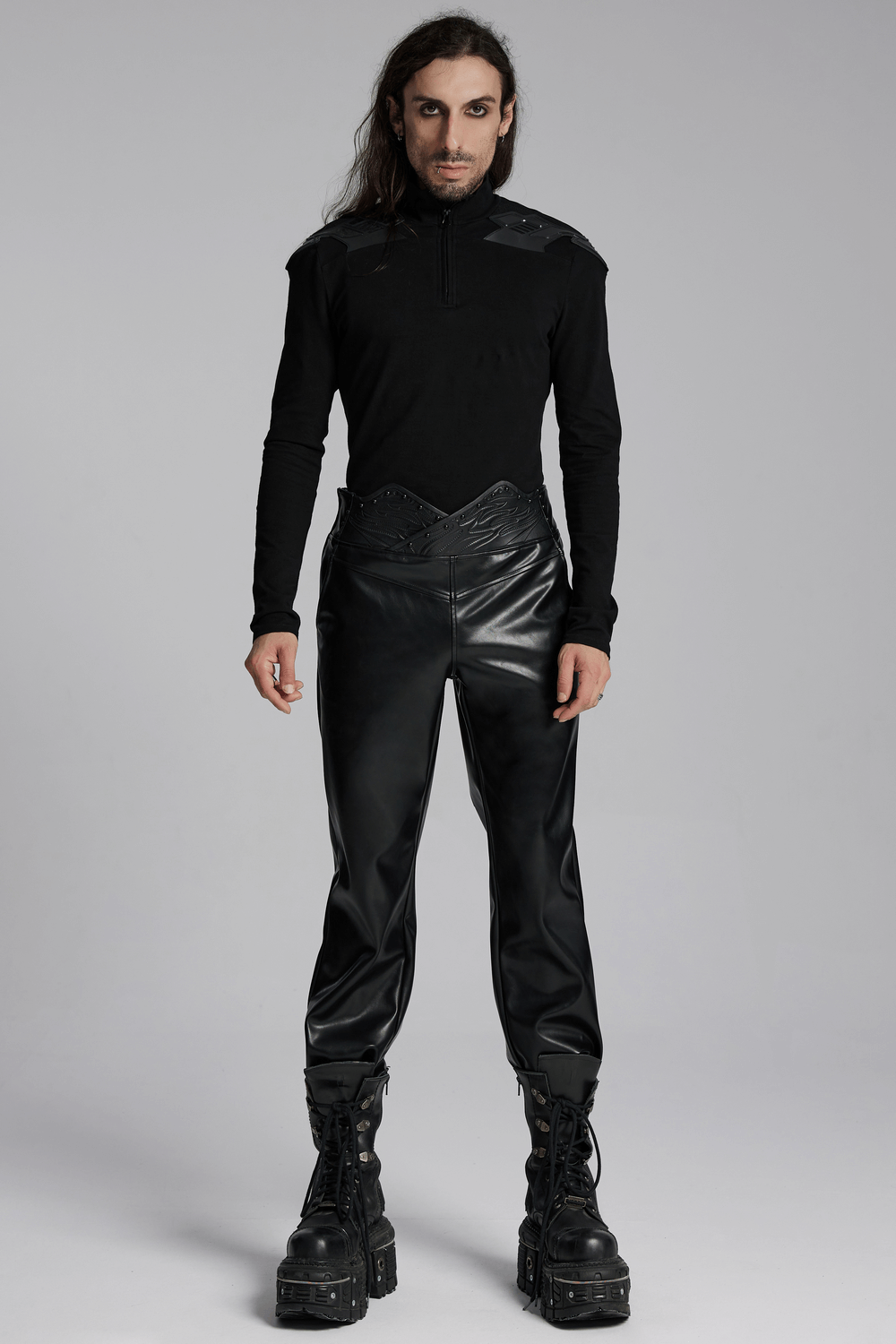 Male model wearing black faux leather punk pants with 3D curved waistband and studded details, paired with combat boots.