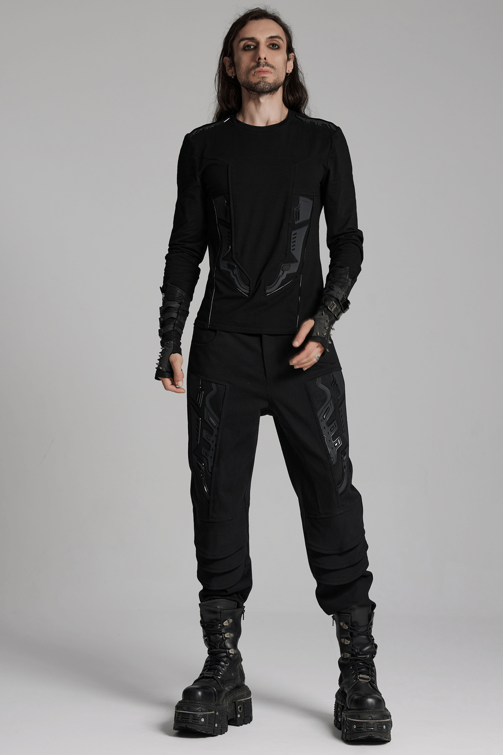 Male model wearing black cyberpunk pants with 3D armor patches, paired with a matching long-sleeve top and chunky boots.