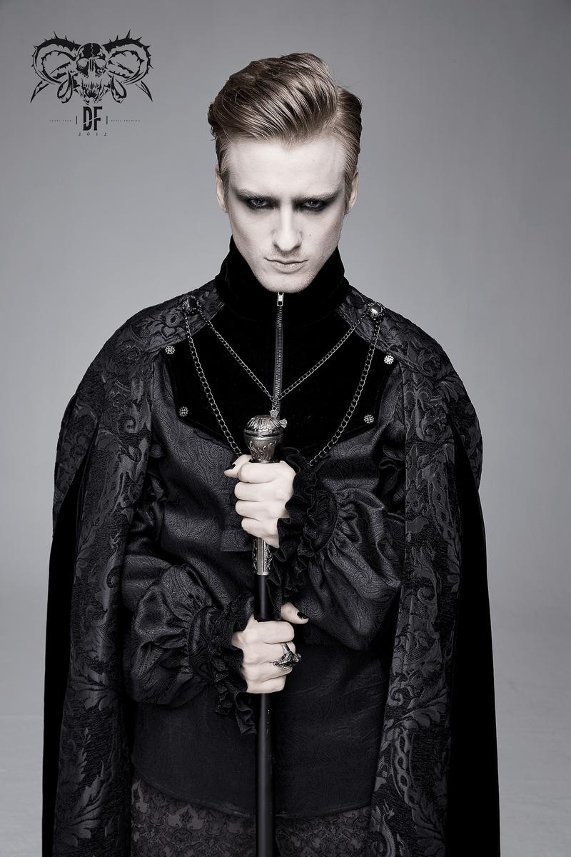 Gothic male model in a black long cloak with a stand-up collar, holding a staff, showcasing elegance and style.