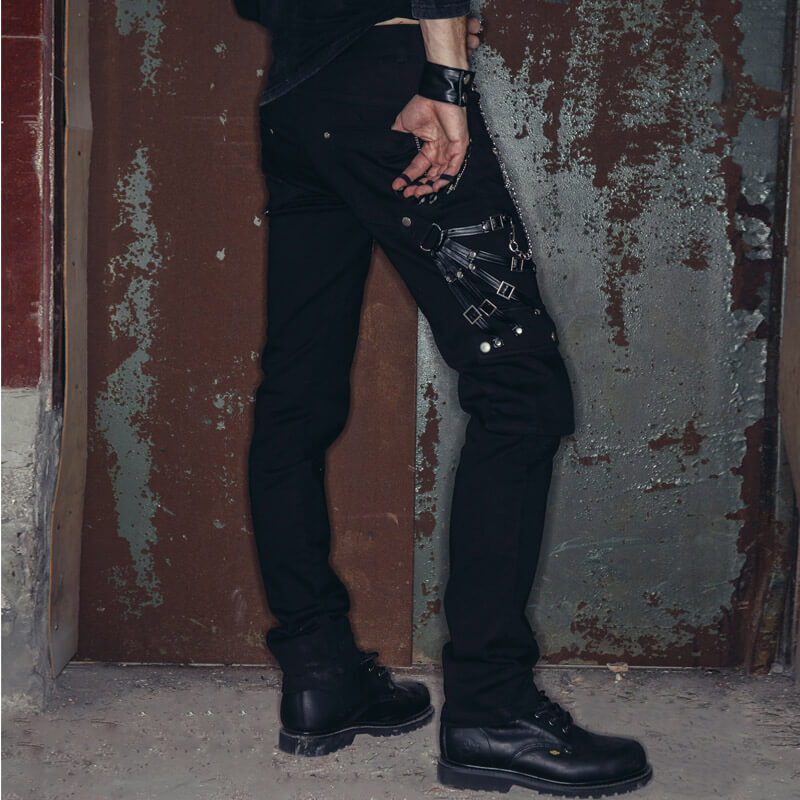 Men's black punk rock pants with zippers and chains displayed against a textured wall.
