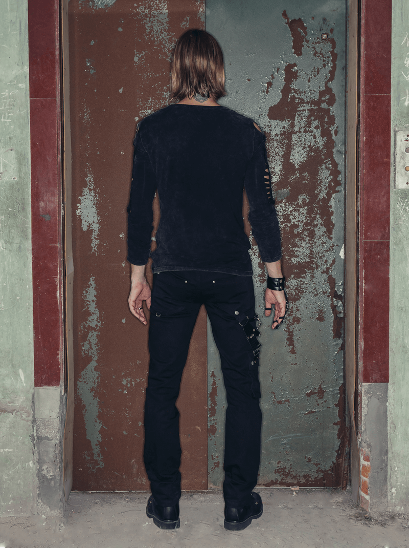 Man wearing black punk rock long pants with chains, seen from behind, standing in front of a rustic door.