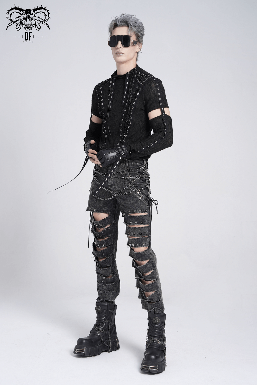 Male model in ripped legs gothic pants with chains and studs, styled with a punk-inspired shirt and bold boots.