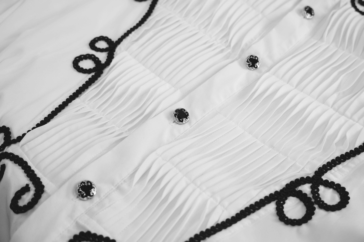 Close-up of a white vintage men's gothic shirt featuring pleats, black lace trim, and decorative buttons.