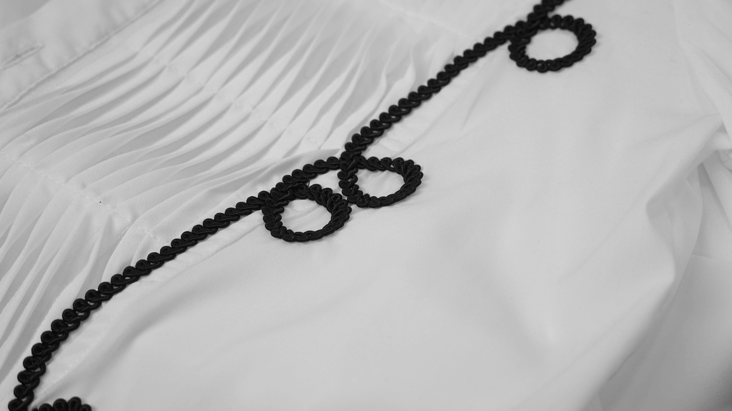 Close-up of a white men's shirt featuring intricate black lace detailing along the collar and pleated fabric.