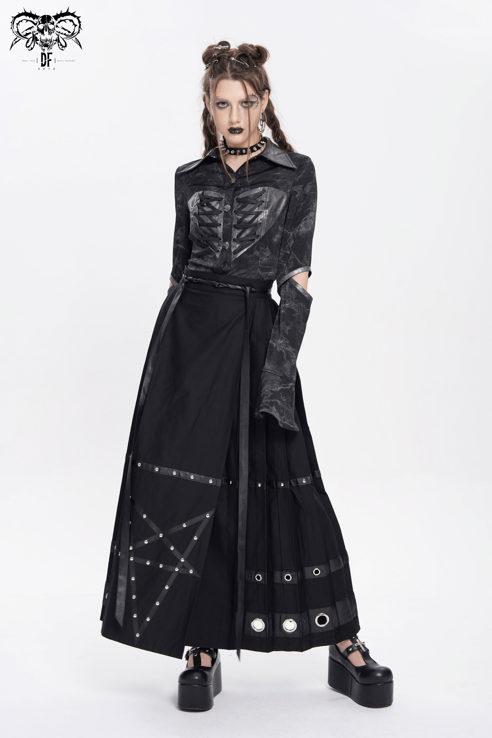 Model wearing a black maxi skirt with pentagram straps and grommet details, styled with a unique shirt and chunky shoes.