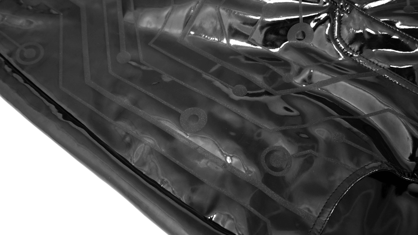 Close-up of glossy black PU leather fabric with a cyberpunk circuit print, highlighting its stylish design.