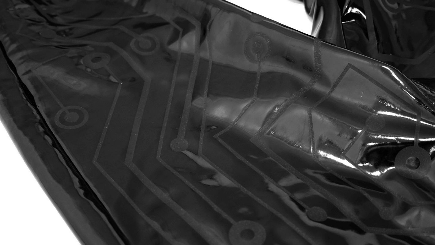 Close-up of black patent leather fabric with cyberpunk circuit print, showcasing sleek style for men's skinny pants.