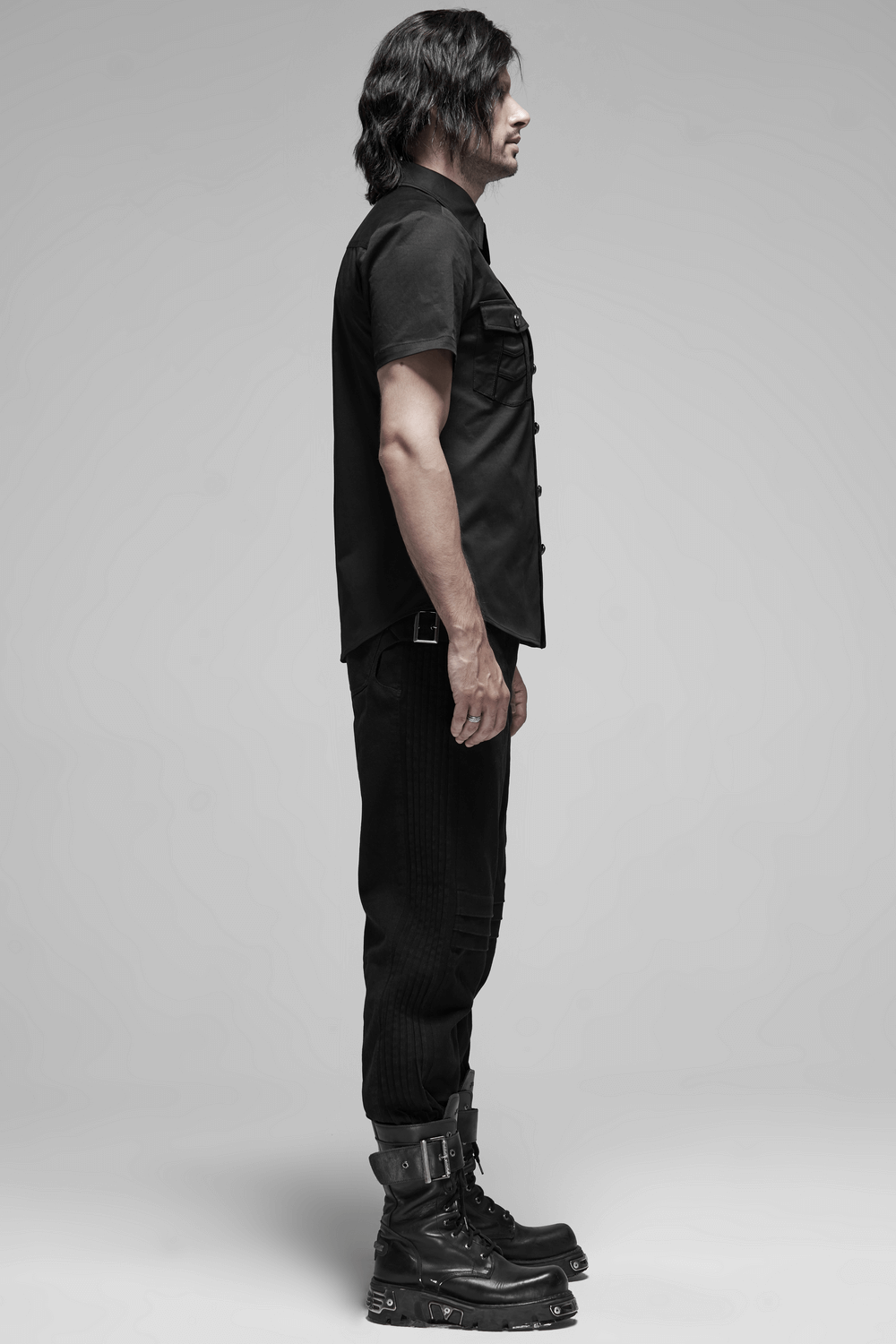 Man in black short-sleeved punk shirt with pockets, styled with edgy black boots, showcasing gothic fashion.