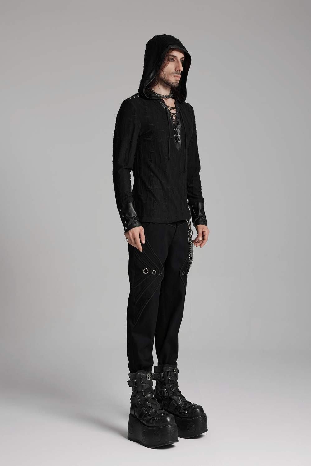 Man wearing a men's dark gothic hooded top with rivet details, showcasing a punk style with lace-up design and striking footwear.