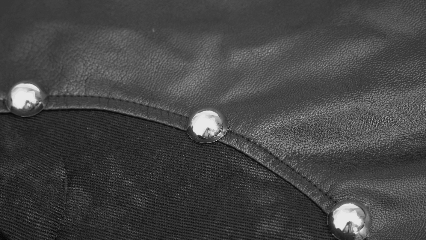 Close-up of black faux leather fabric with silver rivets, showcasing punk style design elements.