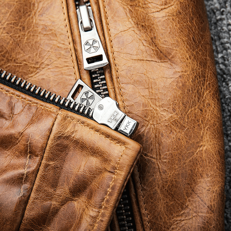 Close-up of silver zipper on a men's yellow-brown leather motorcycle jacket, showcasing vintage style and quality craftsmanship.