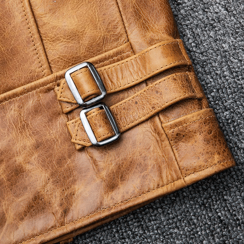 Close-up of men's genuine leather motorcycle jacket showing stylish silver buckles and retro yellow-brown leather texture.