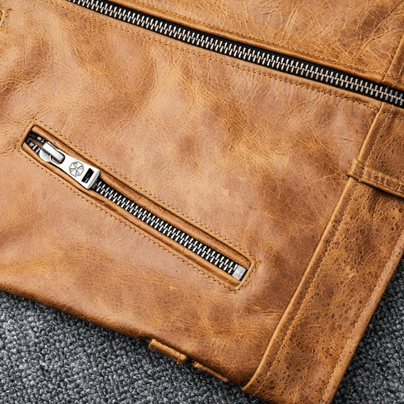 Close-up of a men's yellow-brown leather motorcycle jacket with silver zipper detail on a textured surface.
