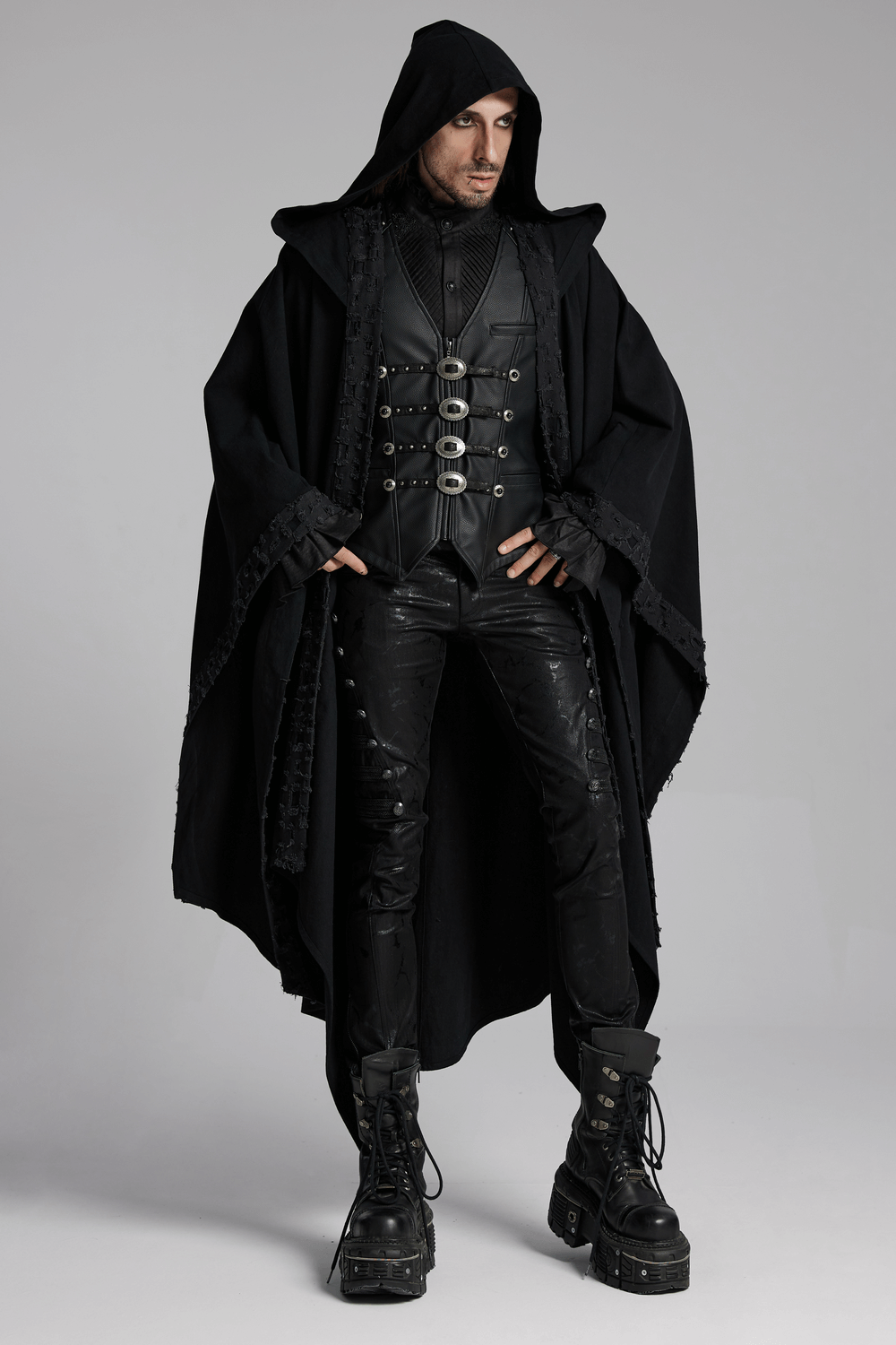 Stylish man in a Gothic faux leather vest with metal buckles, wearing a dramatic black cloak and chunky boots.