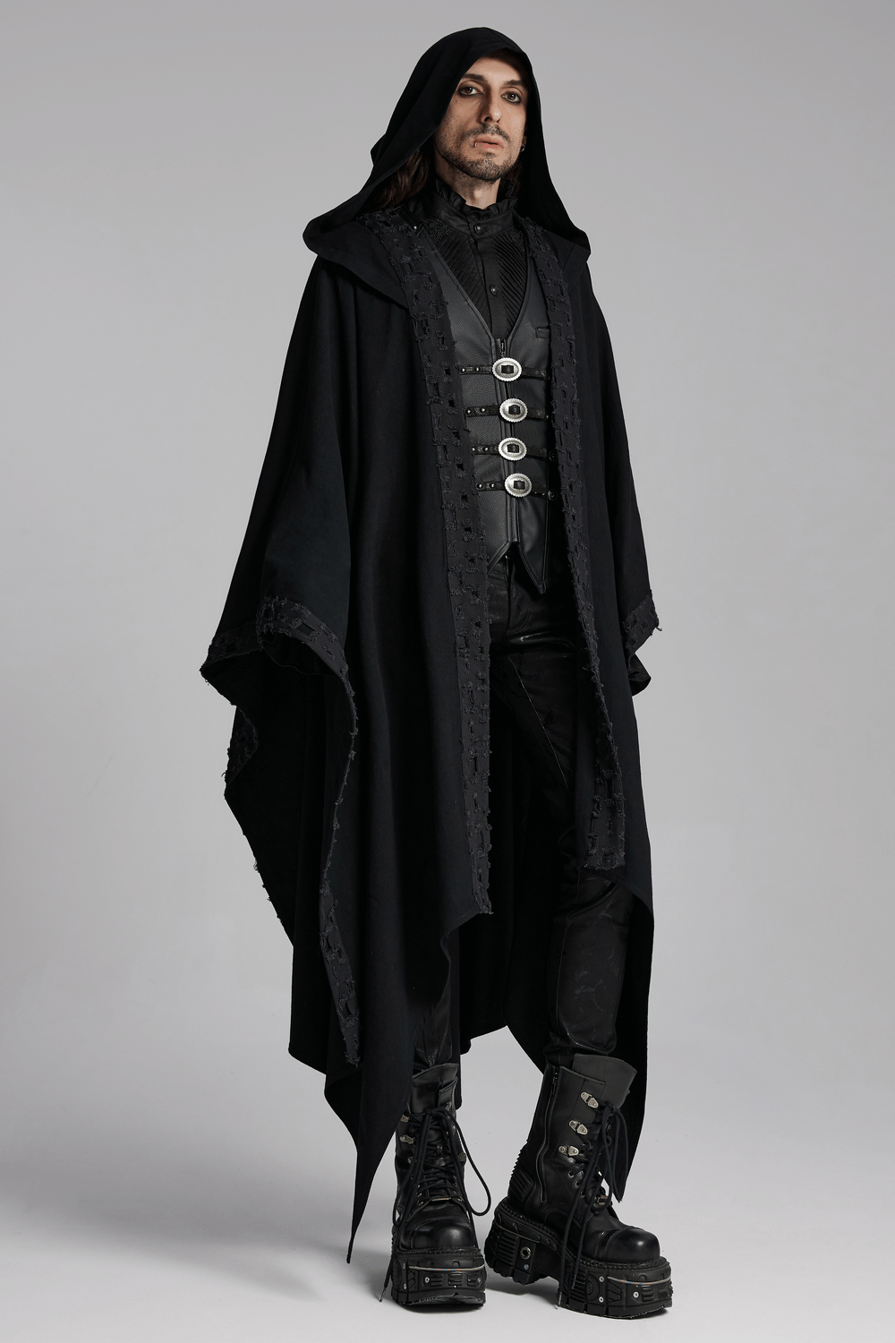 Stylish man in black Gothic attire with a hooded cape and faux leather vest featuring metal buckles and punk vibes.