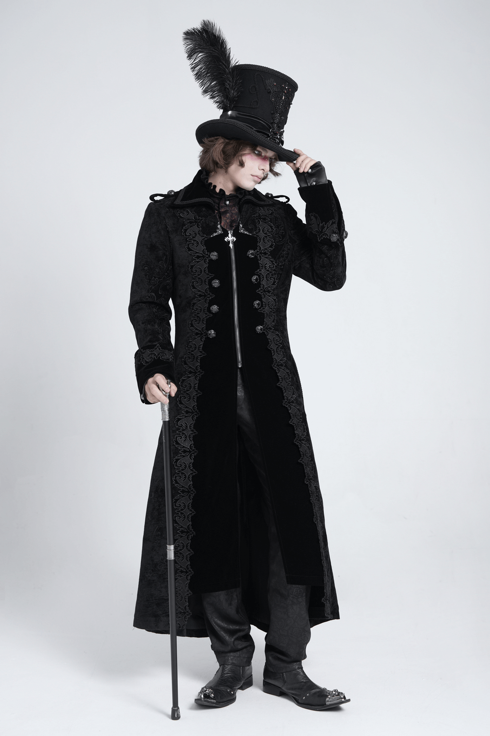 Stylish men's gothic long velvet coat with brocade trim and top hat, posing elegantly with a cane.