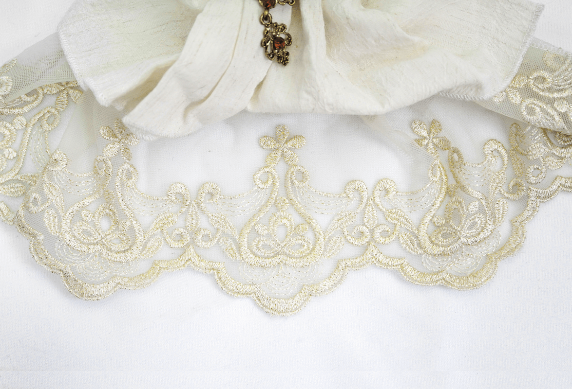Elegant white fabric with intricate gold lace detailing and a vintage brooch accent.