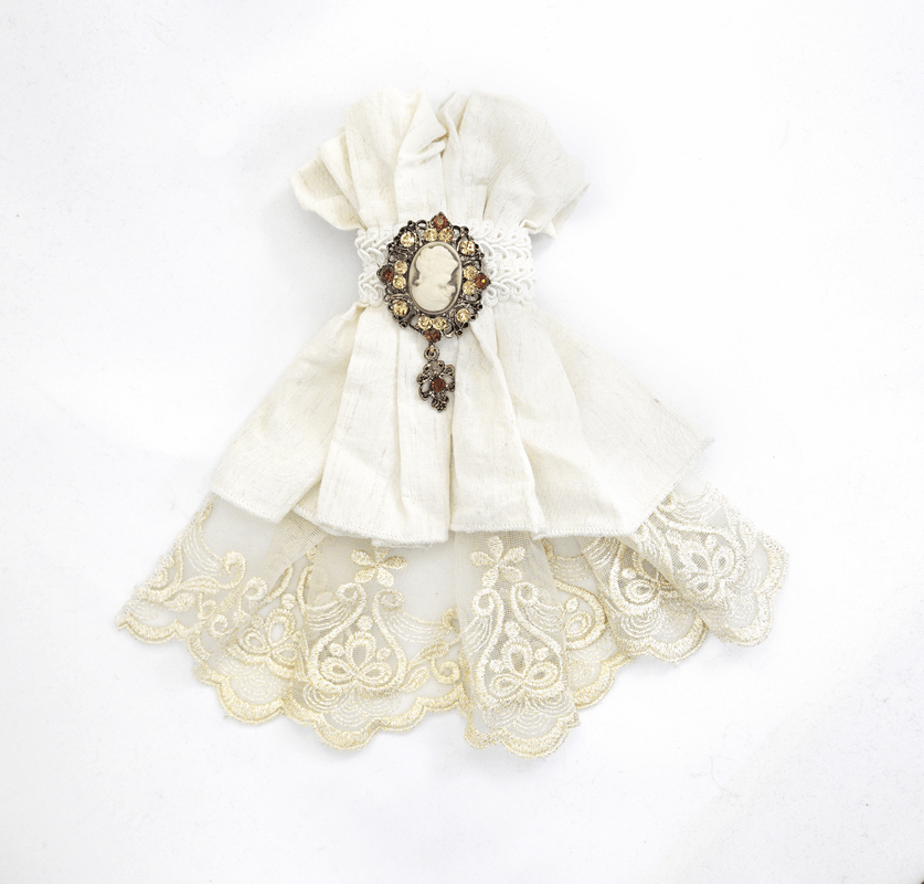 Vintage white lace dress with antique brooch, perfect for dolls or as a unique fashion accessory.