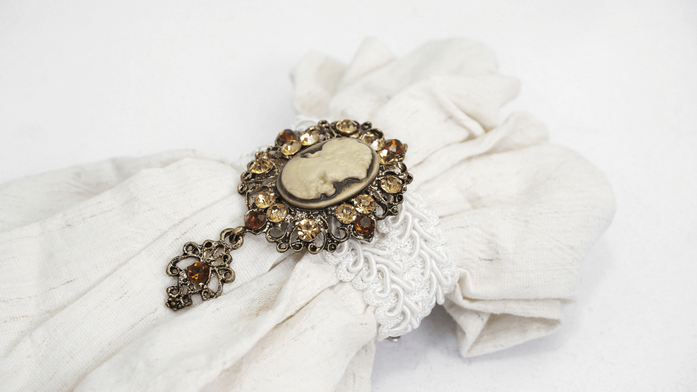Close-up of a vintage brooch with intricate detailing on a white cotton fabric, perfect for gothic fashion.