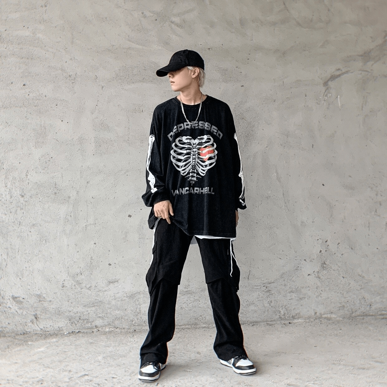 Stylish man in punk-inspired oversized black sweatshirt with skeleton print, paired with trendy baggy pants and cap.