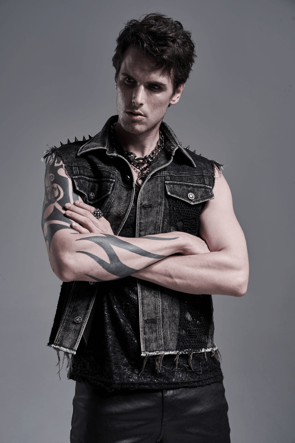Stylish man wearing a men's punk denim vest with rivets and patches, showcasing a rebellious street style.