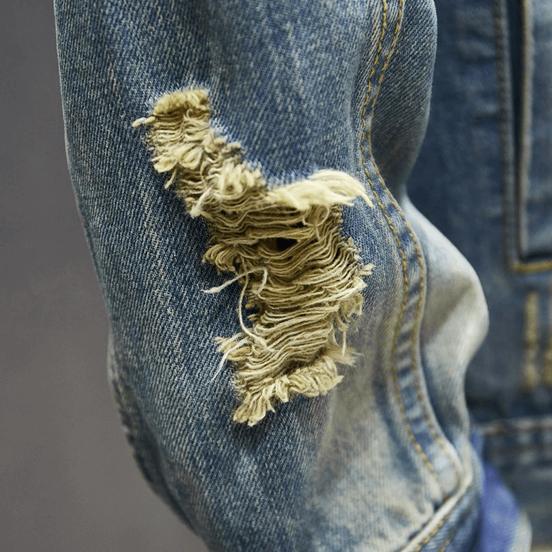 Close-up of a ripped denim jacket sleeve showcasing stylish abrasions for a vintage look.