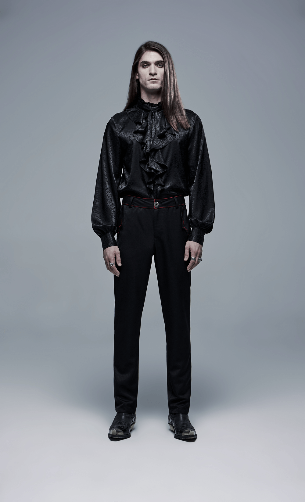 Men in a black ruffled shirt and tailored trousers, embodying a gothic style with a modern twist.