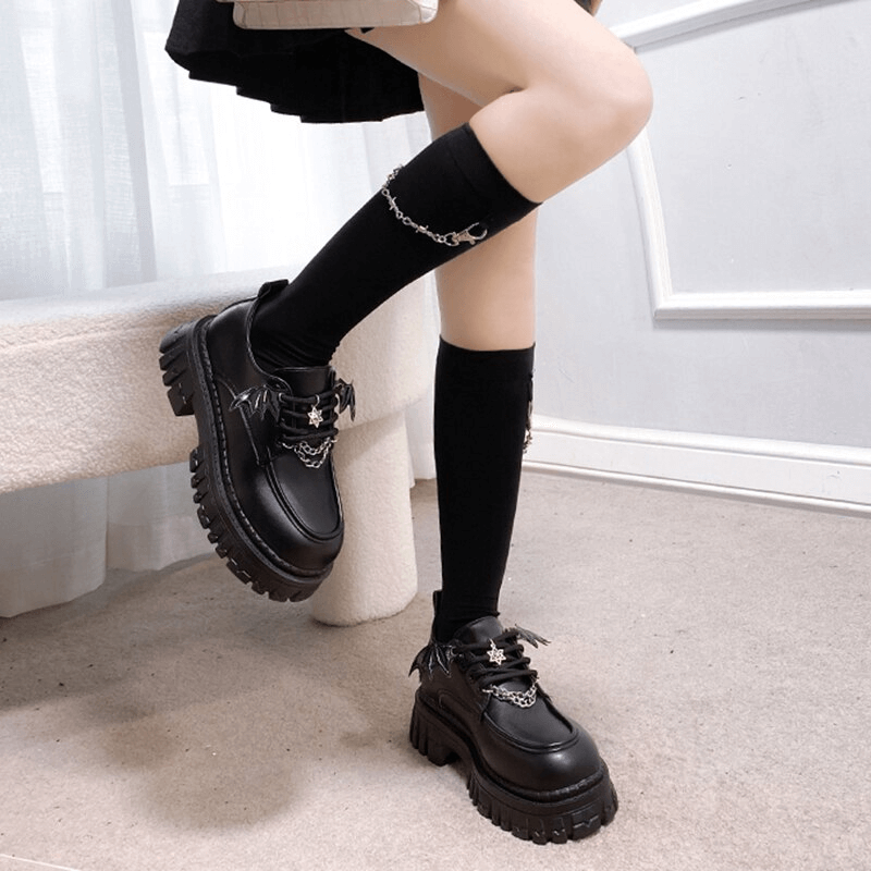 Women's gothic bat wing platform shoes with chunky soles and metal chain detail, styled with knee-high socks.
