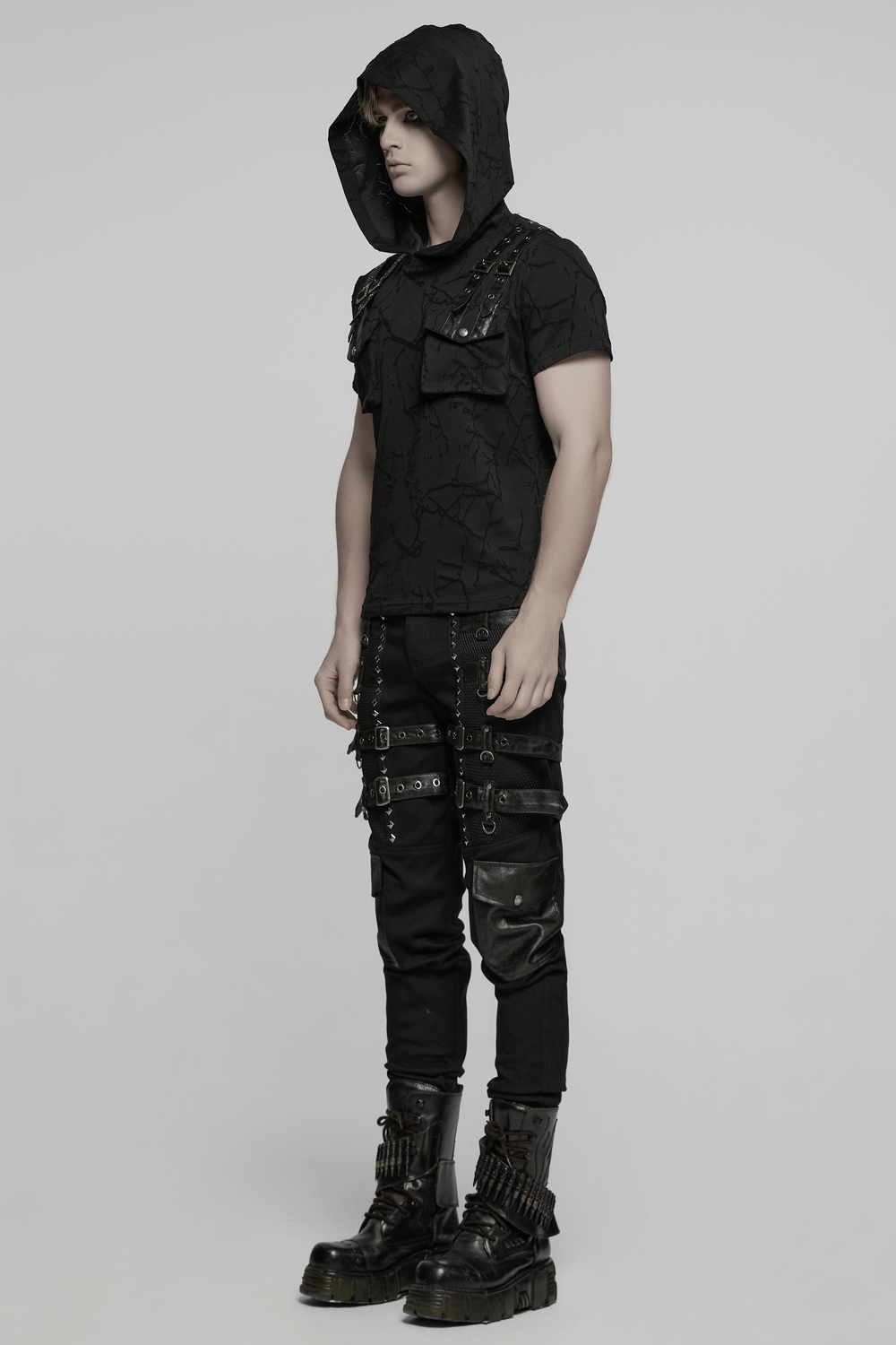 Stylish model in black metal punk outfit featuring studded pants, hooded top, and edgy boots.
