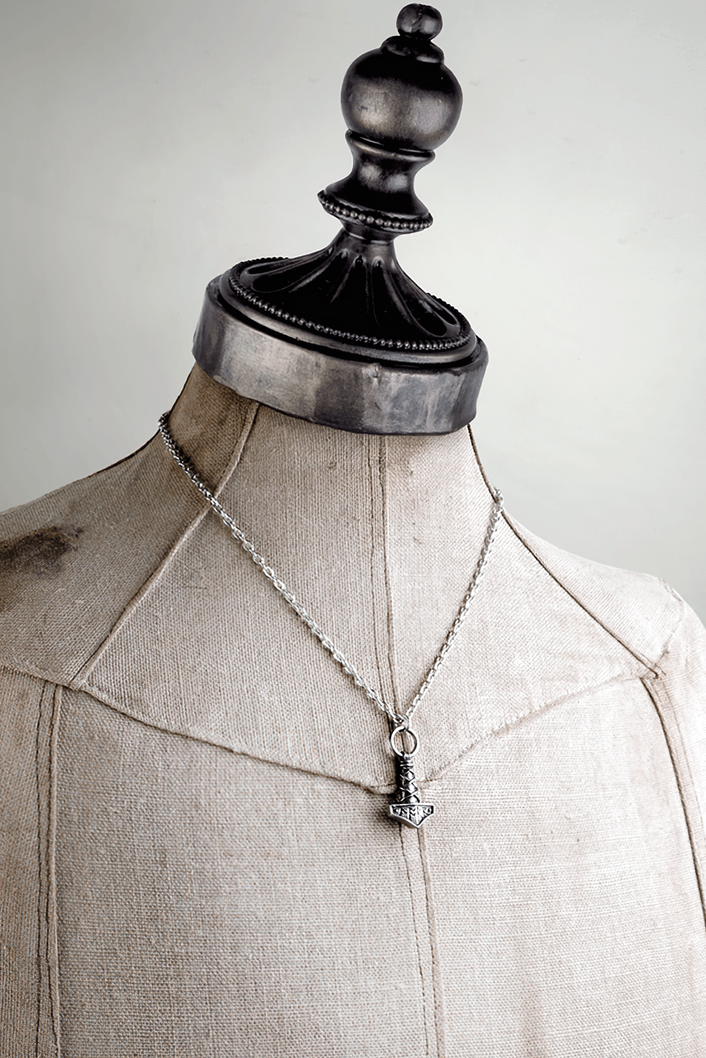 Mini Norse Mjolnir pendant on a silver chain displayed on a dress form, showcasing Viking-style runic detailing.