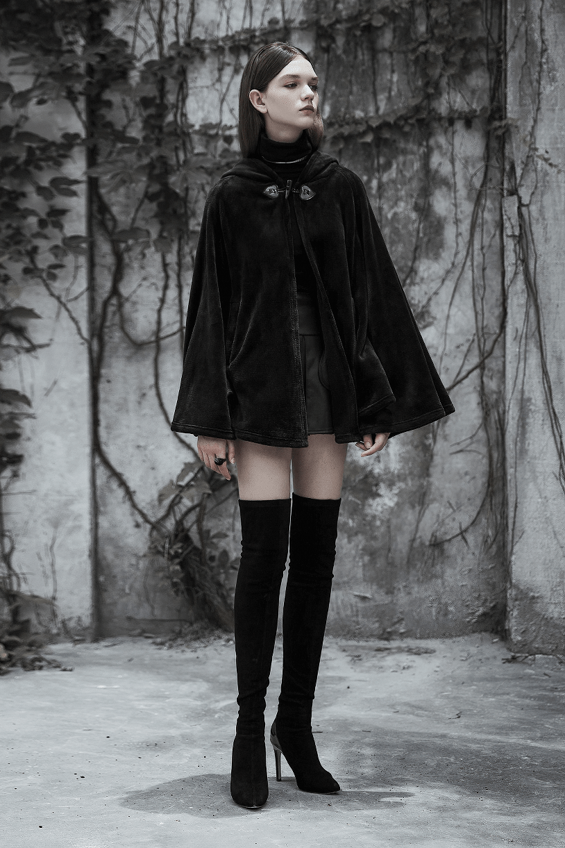 Model wearing a dark velvet embroidered cloak jacket in a moody urban setting.