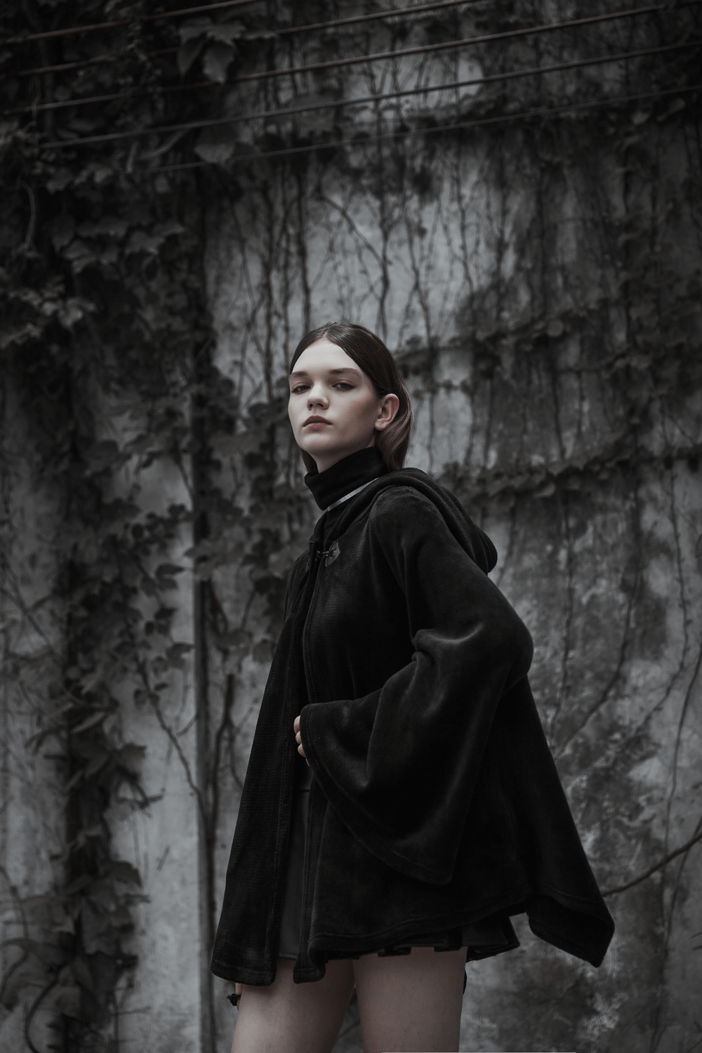 Model wearing a moon embroidered dark velvet hooded cloak jacket against a moody backdrop.