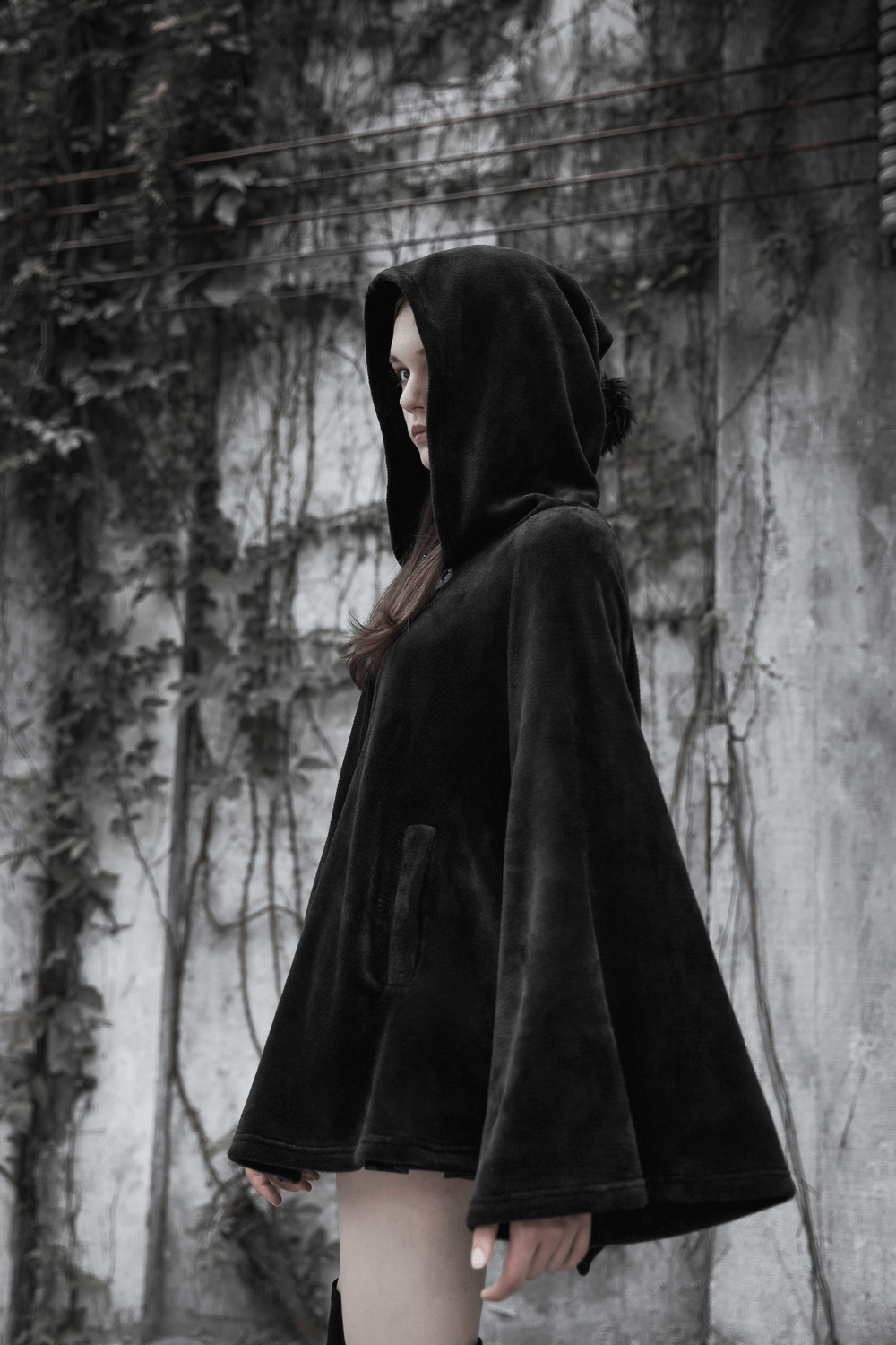 Model wearing a moon embroidered dark velvet hooded cloak jacket, showcasing gothic elegance against a textured backdrop.