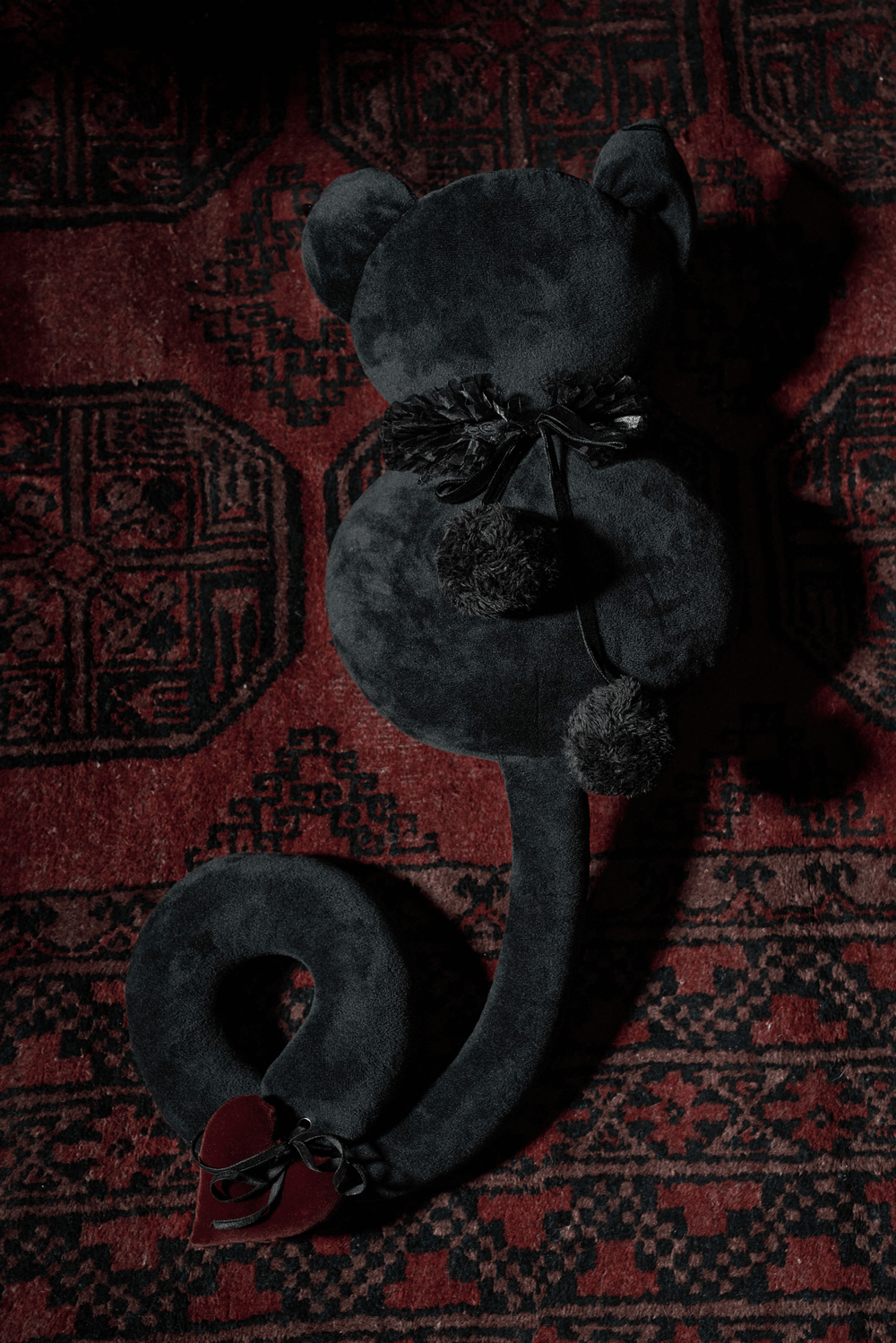 Mystic black plush cat toy with detachable hearts and lace collar on a patterned rug.