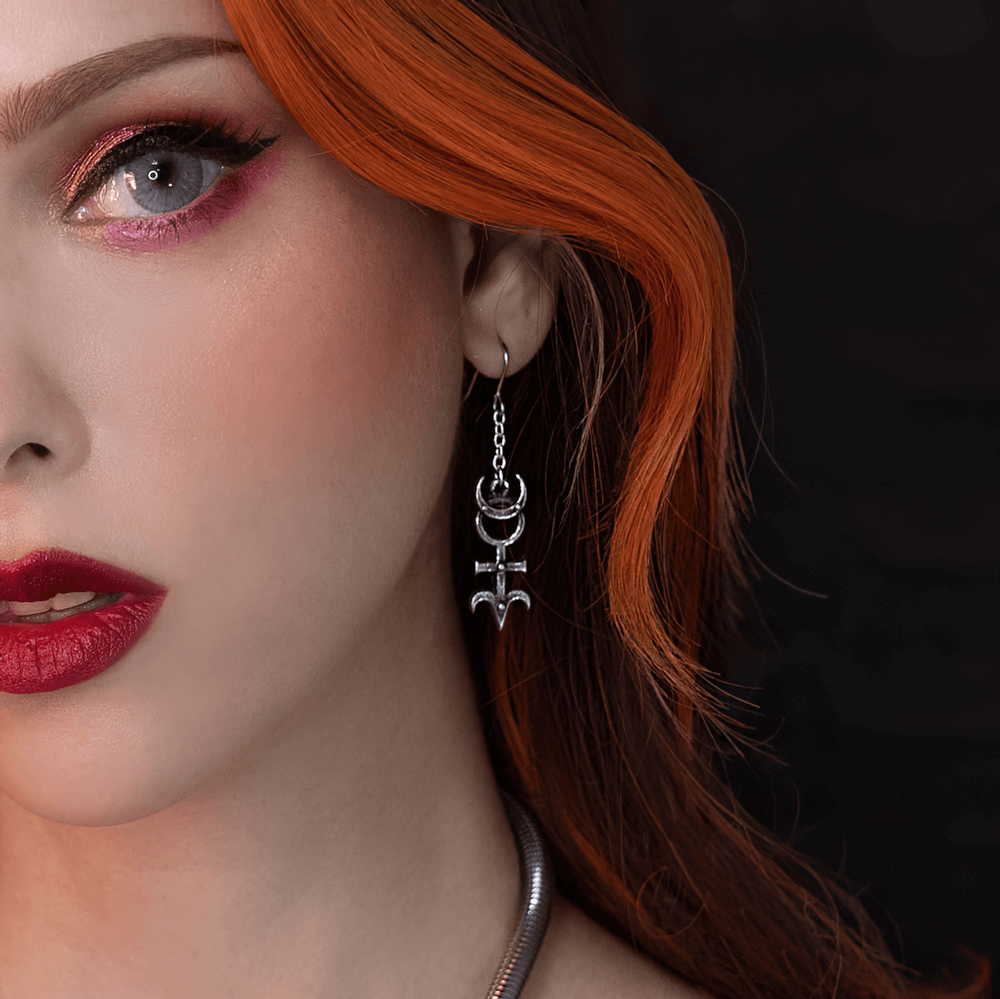 Occult Pewter Moon and Monad Symbol Drop Earrings showcased on a model with striking makeup and flowing red hair.