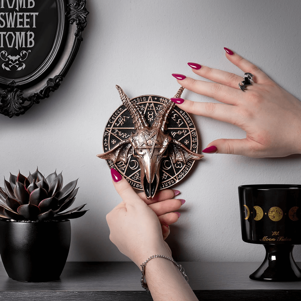 Hand holding an occult ram skull wall plaque with pentagram design, showcasing gothic home decor accents.