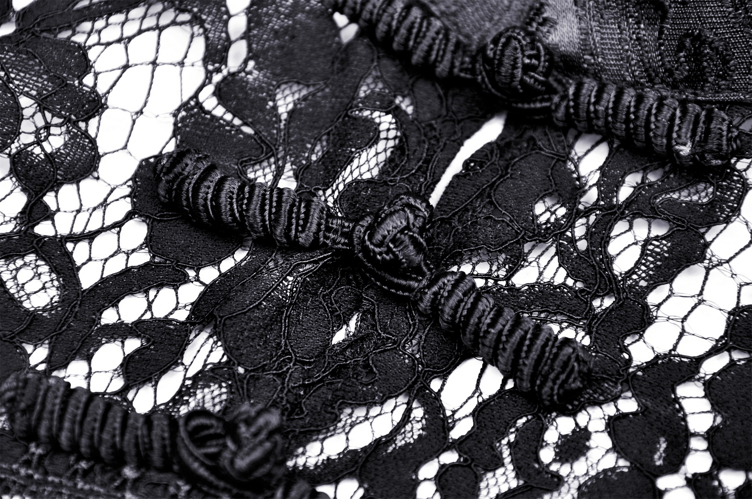 Close-up of intricate black lace fabric with ribbon details, highlighting elegance and sophistication.